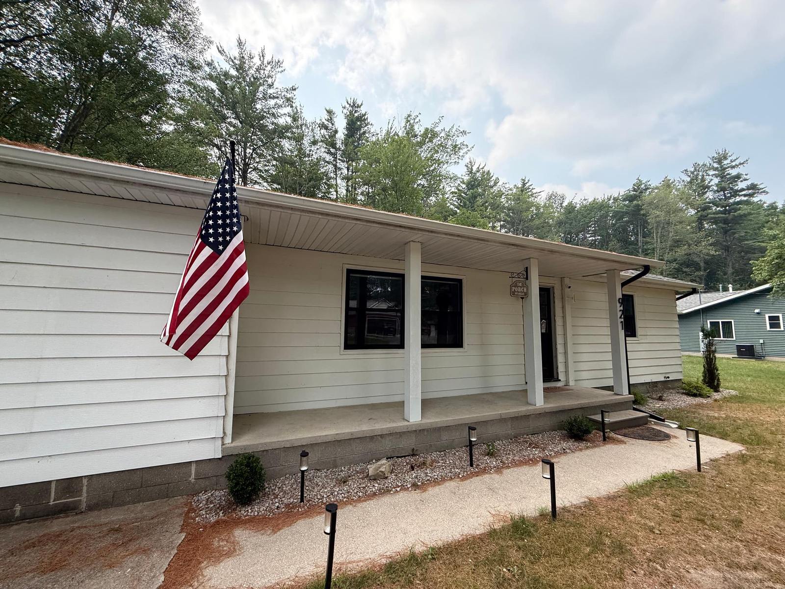 White single-level cottage with a covered front porch under tall pines