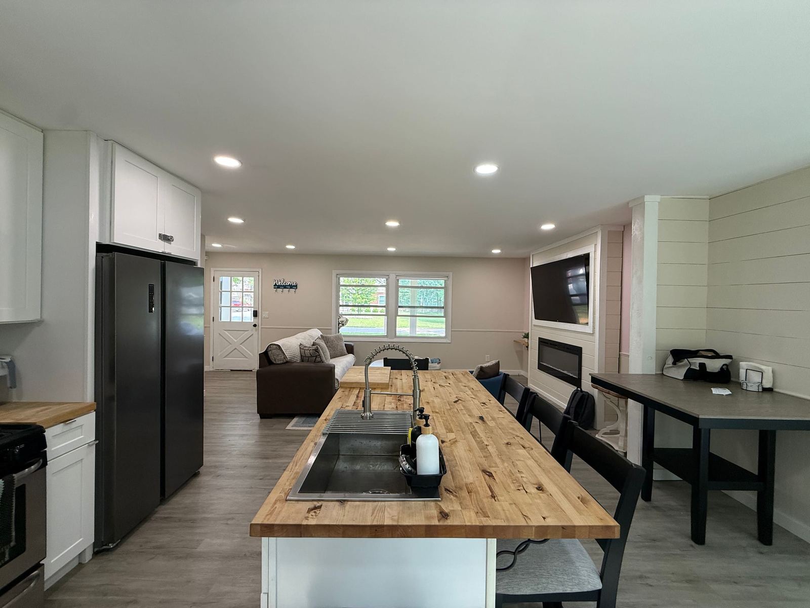 Open kitchen and living room with a butcher-block island, stainless appliances, and a TV above the fireplace