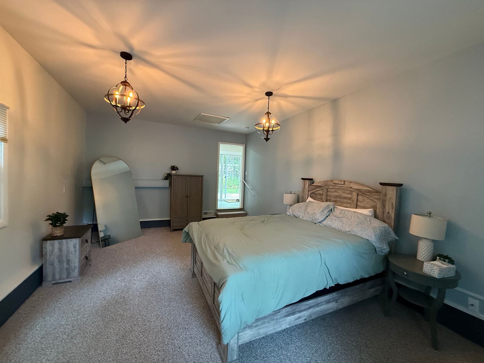 Primary bedroom with a rustic wood bed, two pendant chandeliers, and a door to the backyard