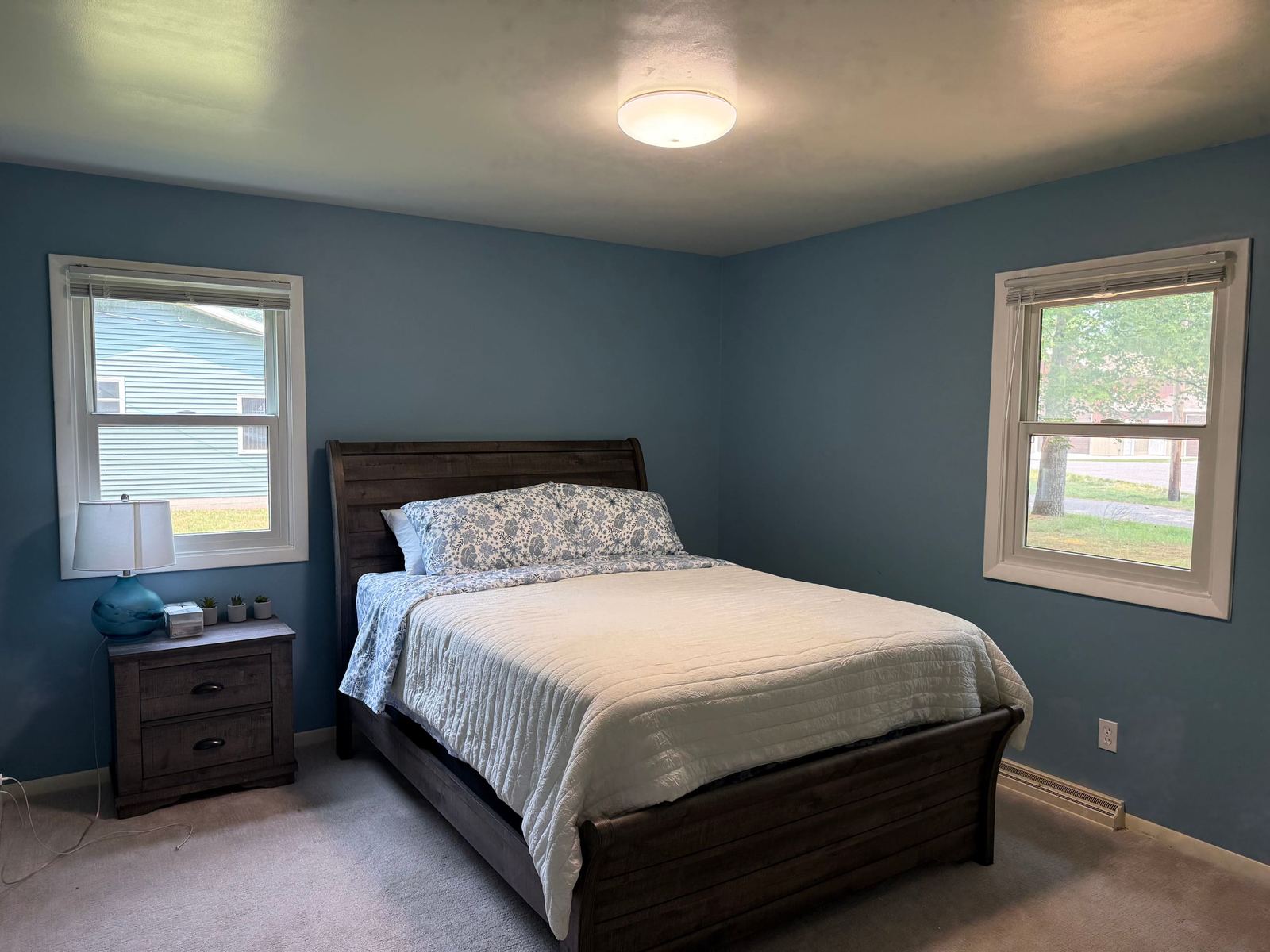 Blue bedroom with a dark wood sleigh bed and windows on two walls